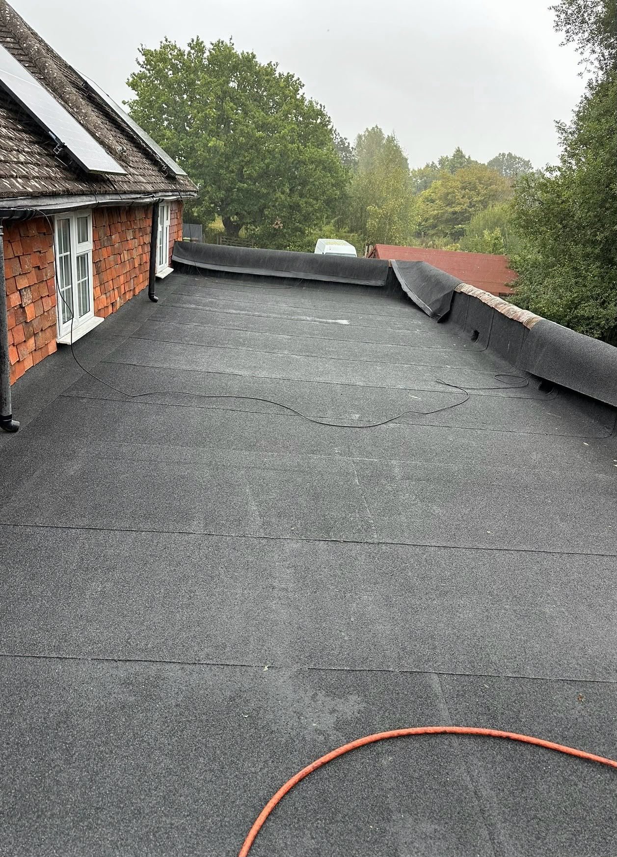 Long flat roof finished in black mineral felt beside a tile-hung cottage