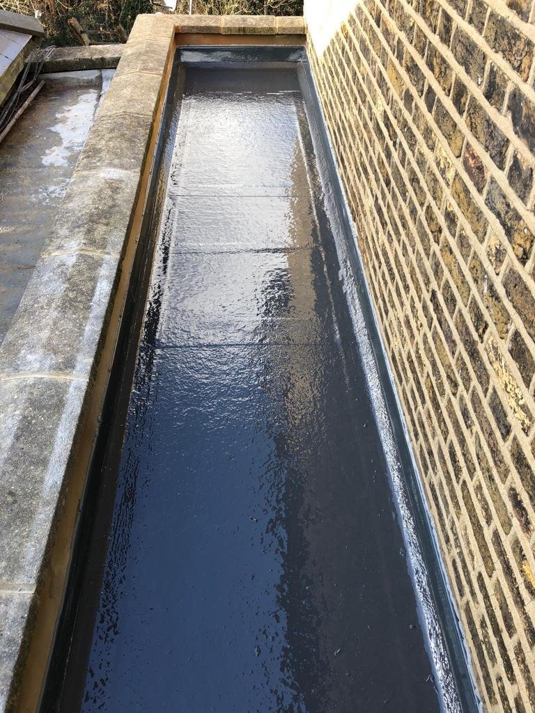 Freshly coated box gutter running along a brick parapet wall